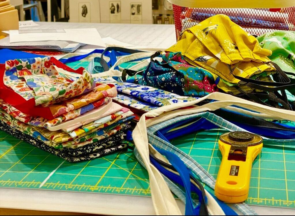 Assorted brightly colored fabric face masks and a yellow rotary cutter lay on a gridded cutting mat.