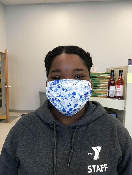 A woman smiles while wearing a blue flowered face mask and a grey YMCA staff sweatshirt.